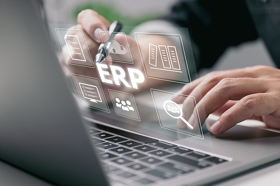 Enterprise Resource Planning (ERP) is a business resource planning software system. On a virtual screen, there is a concept of a hand typing computer laptop icons.